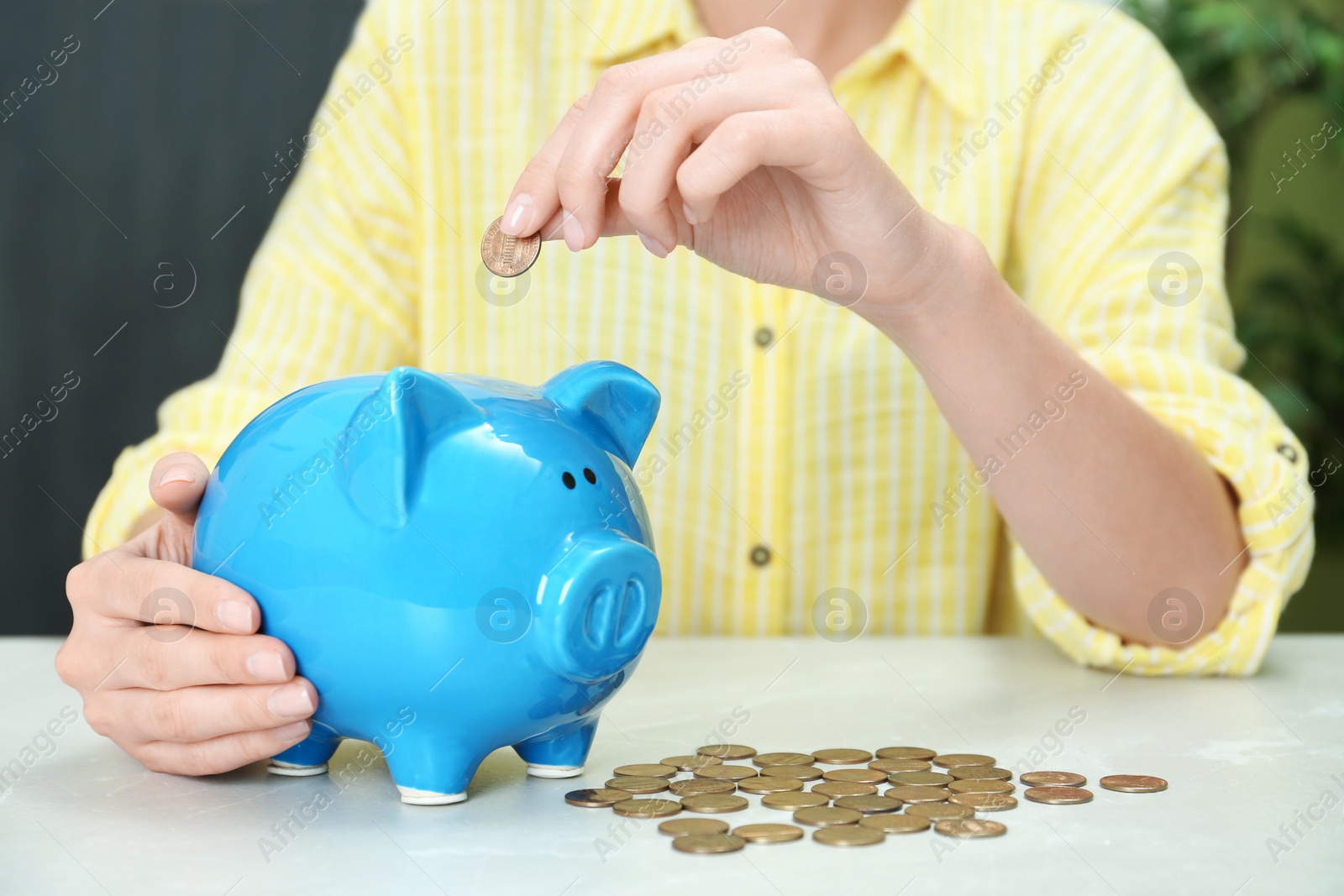 Photo of Woman putting coin into piggy bank at light table, closeup