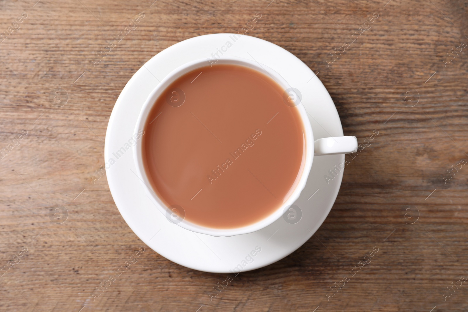 Photo of Delicious tea with milk in white cup on wooden table, top view