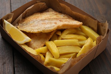 Delicious fish and chips in paper box on wooden table, closeup