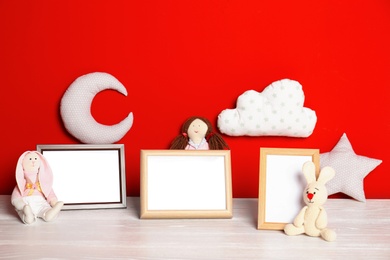 Photo of Soft toys and photo frames on table against red background, space for text. Child room interior