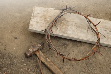 Photo of Crown of thorns, hammer with nails and wooden plank on ground, above view. Easter attributes