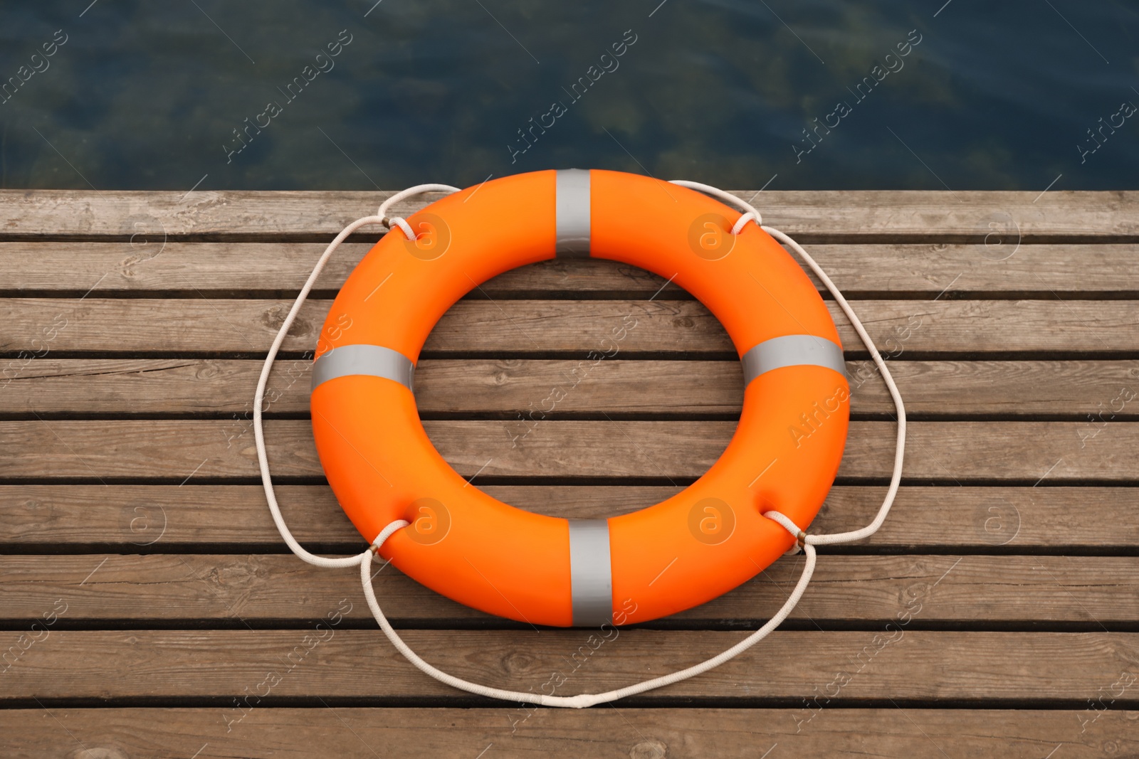 Photo of Orange lifebuoy on wooden pier near water. Rescue equipment