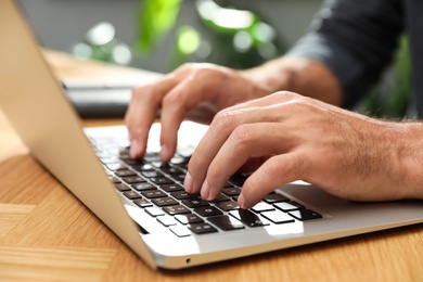 Man using laptop for search at wooden table indoors, closeup