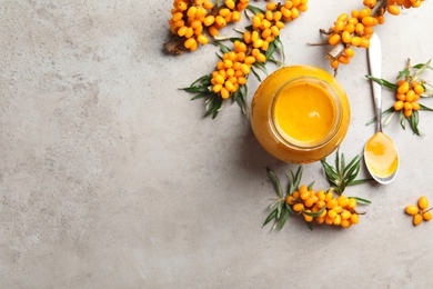 Delicious sea buckthorn jam and fresh berries on grey table, flat lay. Space for text