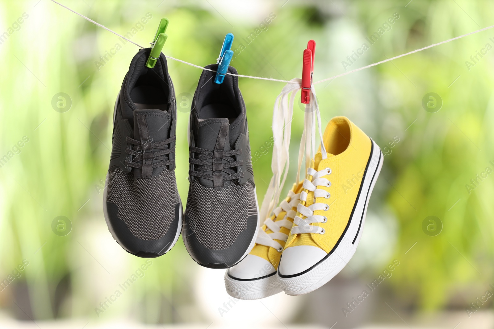 Photo of Different stylish sneakers drying on washing line against blurred background