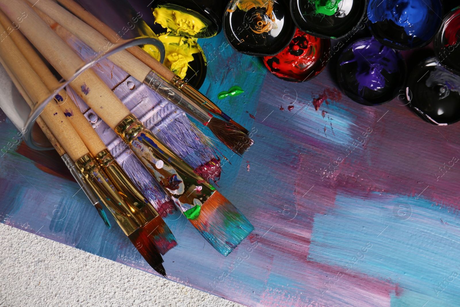 Photo of Canvas with colorful abstract painting and different brushes, top view