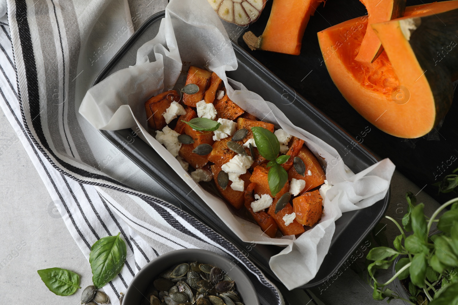 Photo of Freshly baked pumpkin pieces with cheese, seeds and basil on light table, flat lay