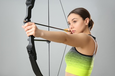 Photo of Sporty young woman practicing archery on light grey background