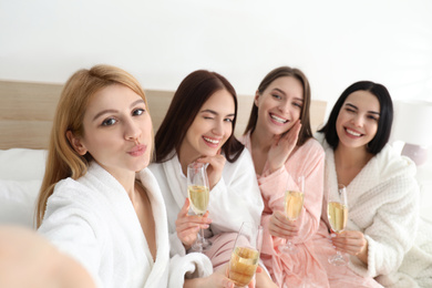 Beautiful young ladies with champagne taking selfie on bed at pamper party. Women's Day