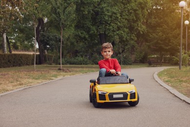 Cute little boy driving children's car outdoors. Space for text