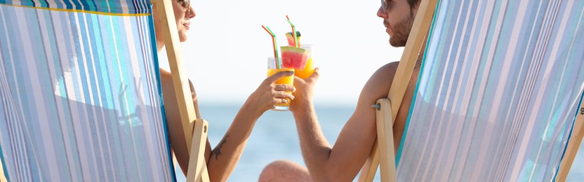 Image of Young couple with cocktails in beach chairs at seacoast. Banner design
