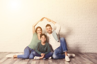 Image of Happy family forming roof with their hands near brick wall. Insurance concept