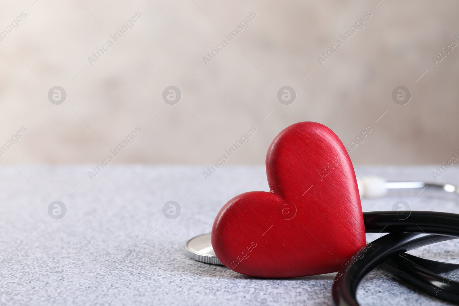 Photo of Stethoscope and red heart on grey stone table, closeup. Space for text