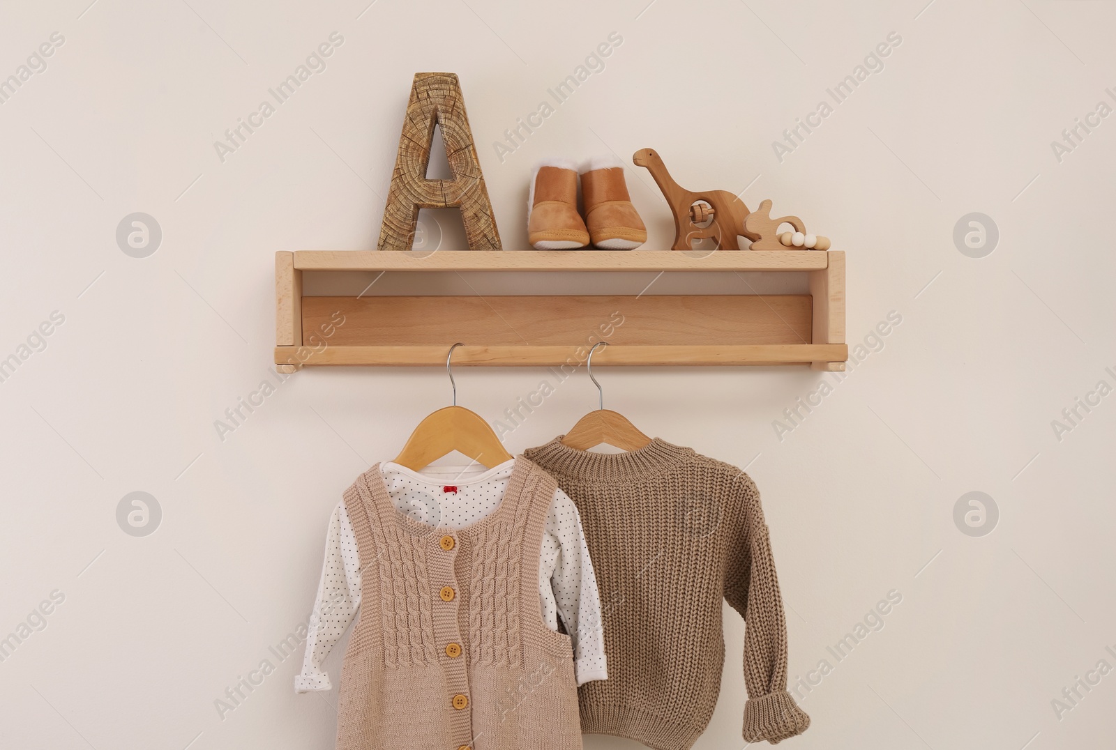 Photo of Wooden shelf with baby clothes and toys on white wall