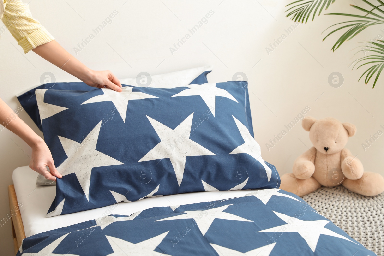 Photo of Woman making bed with stylish linens in children's room, closeup