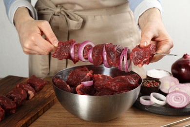 Photo of Woman stringing marinated meat on skewer at wooden table, closeup