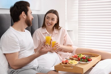 Happy couple having breakfast and talking on bed at home