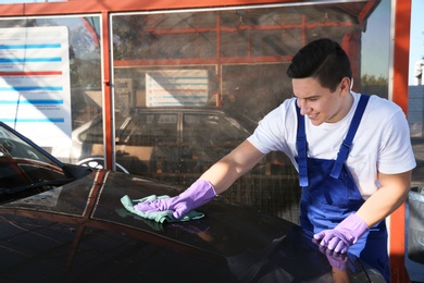 Photo of Worker cleaning automobile with rag at car wash