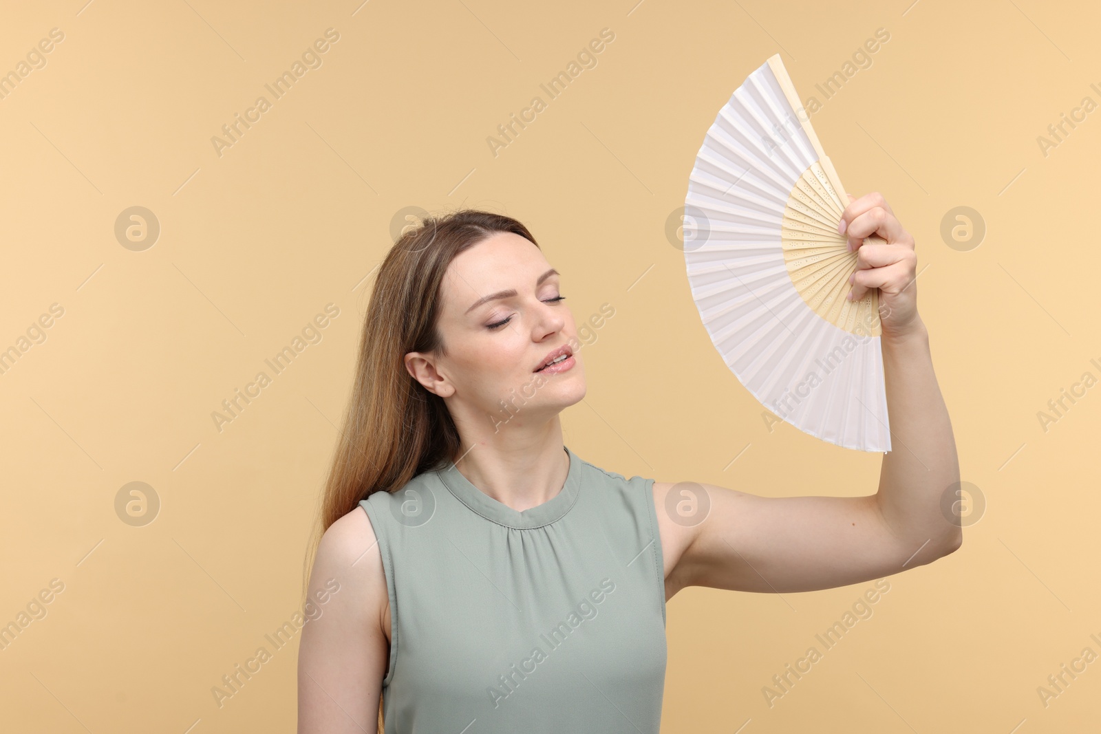 Photo of Beautiful woman waving hand fan to cool herself on beige background