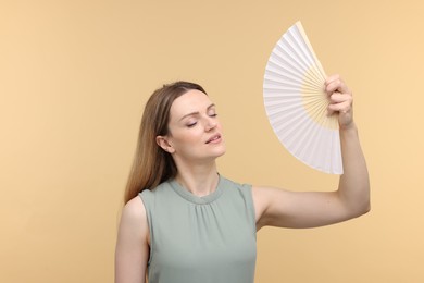 Beautiful woman waving hand fan to cool herself on beige background