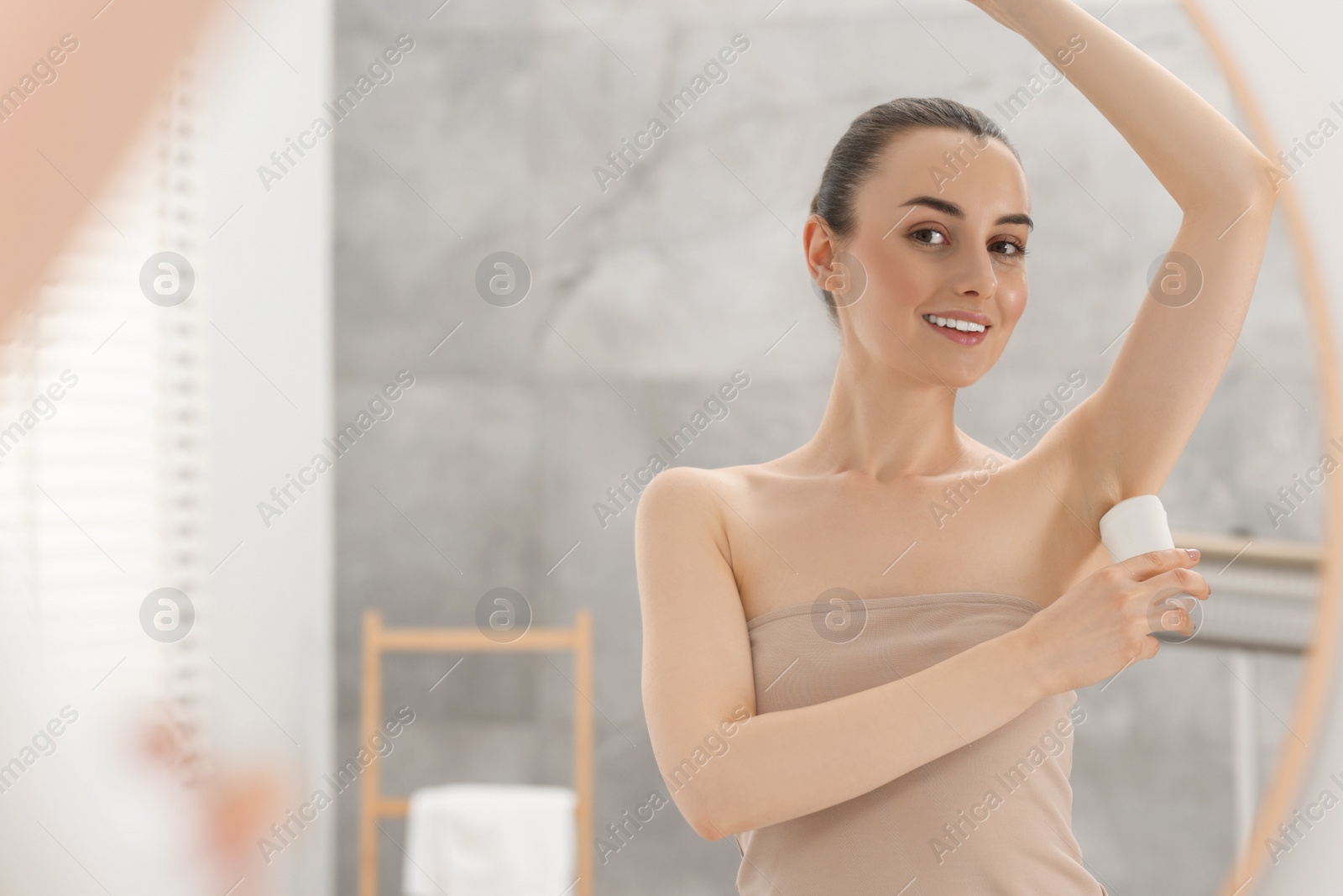 Photo of Beautiful woman applying deodorant near mirror in bathroom