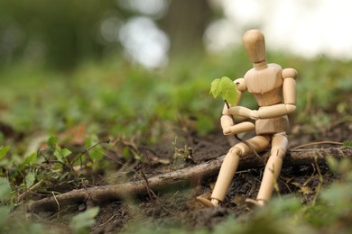 Wooden human figure with young green seedling on soil outdoors, space for text