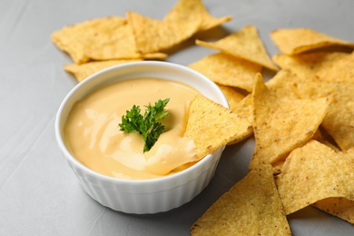 Photo of Tasty cheese sauce with Mexican nachos chips on grey table, closeup