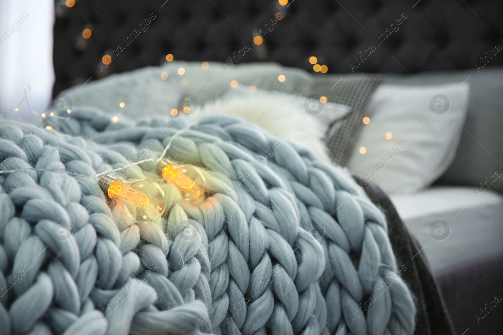 Photo of Knitted plaid and garland on bed, closeup. Modern interior element