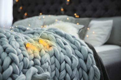 Photo of Knitted plaid and garland on bed, closeup. Modern interior element
