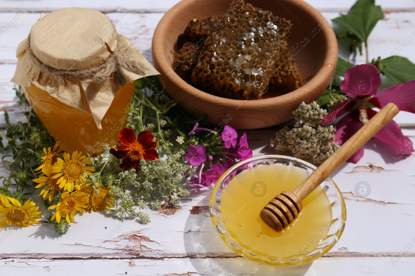 Photo of Delicious honey, combs and different flowers on white wooden table