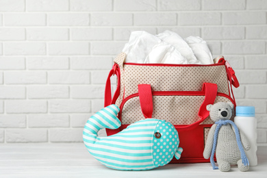 Bag with diapers and baby accessories on wooden table against white brick wall