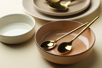 Photo of Stylish empty dishware and spoons on beige background, closeup