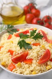 Photo of Tasty couscous with parsley, corn and tomatoes in bowl on table, closeup