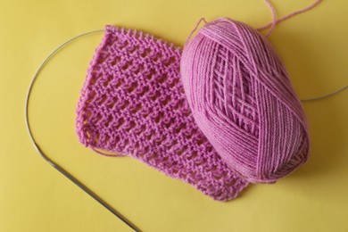Photo of Pink knitting, yarn and needle on yellow background, top view