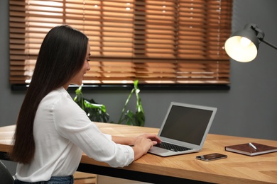 Photo of Young woman using laptop for search at wooden table in office