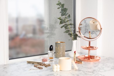 Photo of Burning soy candles, cosmetics and stylish accessories on white window sill indoors