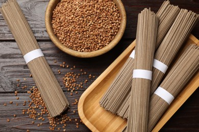 Uncooked buckwheat noodles (soba) and grains on wooden table, flat lay
