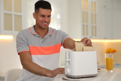 Man using toaster at table in kitchen