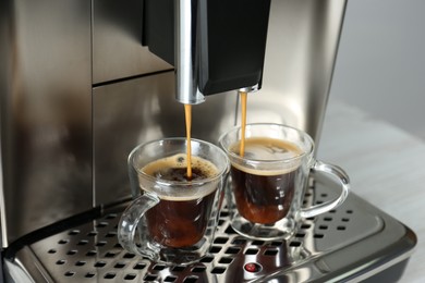 Photo of Modern espresso machine pouring coffee into glass cups on table, closeup