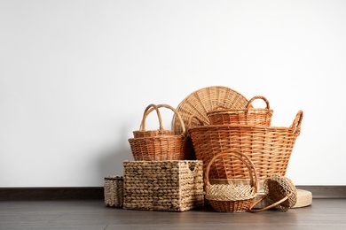 Photo of Many different wicker baskets made of natural material on floor near light wall