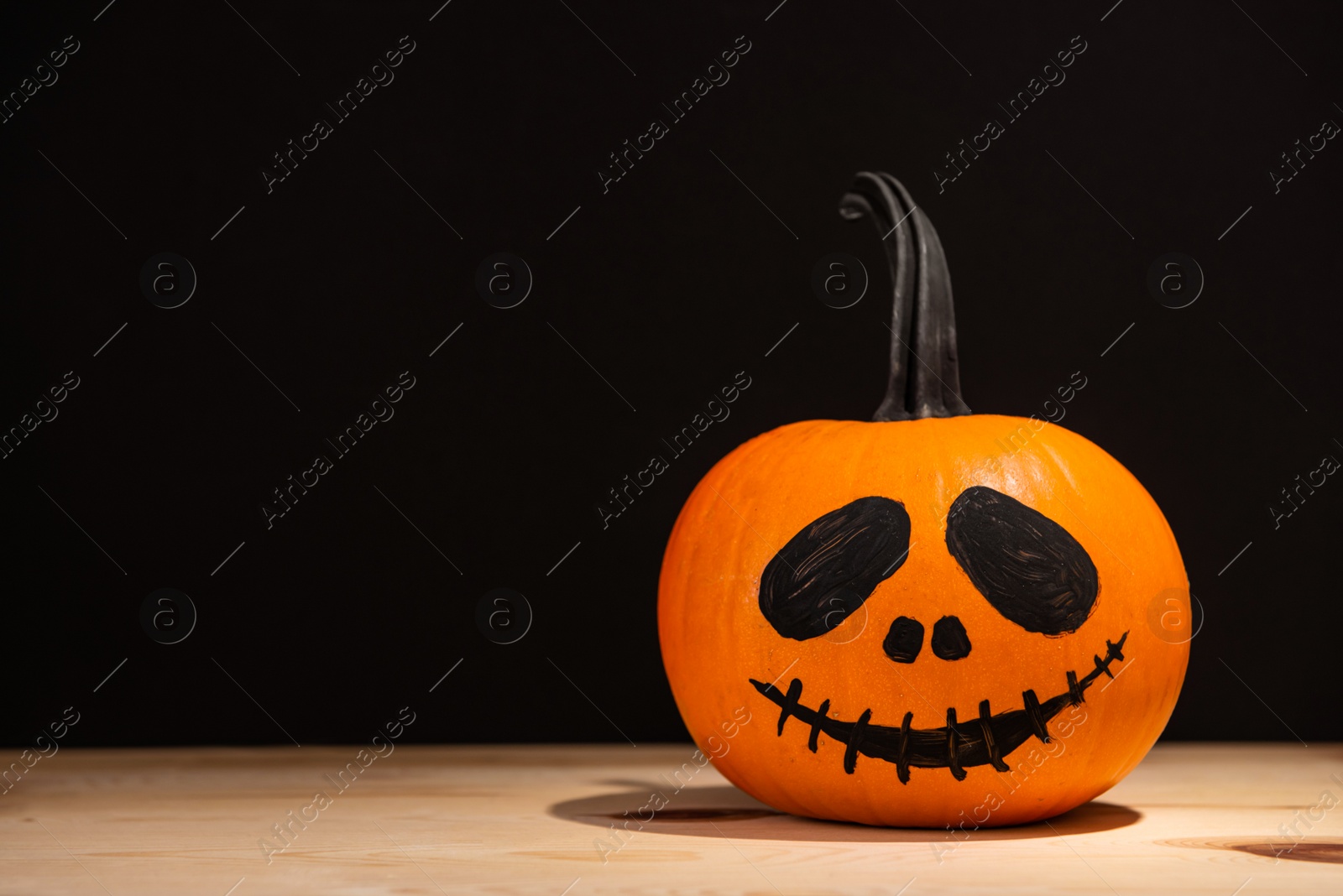 Photo of Halloween celebration. Pumpkin with drawn face on wooden table against black background, space for text