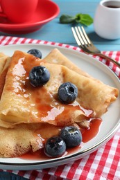 Delicious crepes served with blueberries and syrup on table, closeup