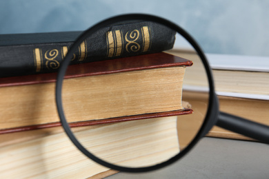 Photo of Looking through magnifying glass at stack of vintage books on grey table, closeup. Search concept