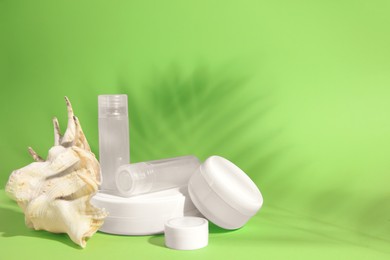 Photo of Jars of cream, shampoo samples, lip balm and seashell on light green background, space for text