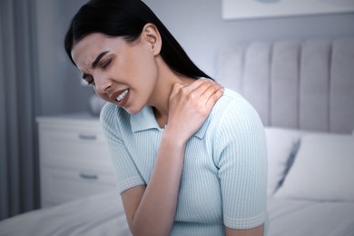 Woman suffering from shoulder pain on bed at home