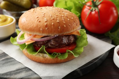 Photo of Tasty hamburger with patty, cheese and vegetables on wooden table, closeup