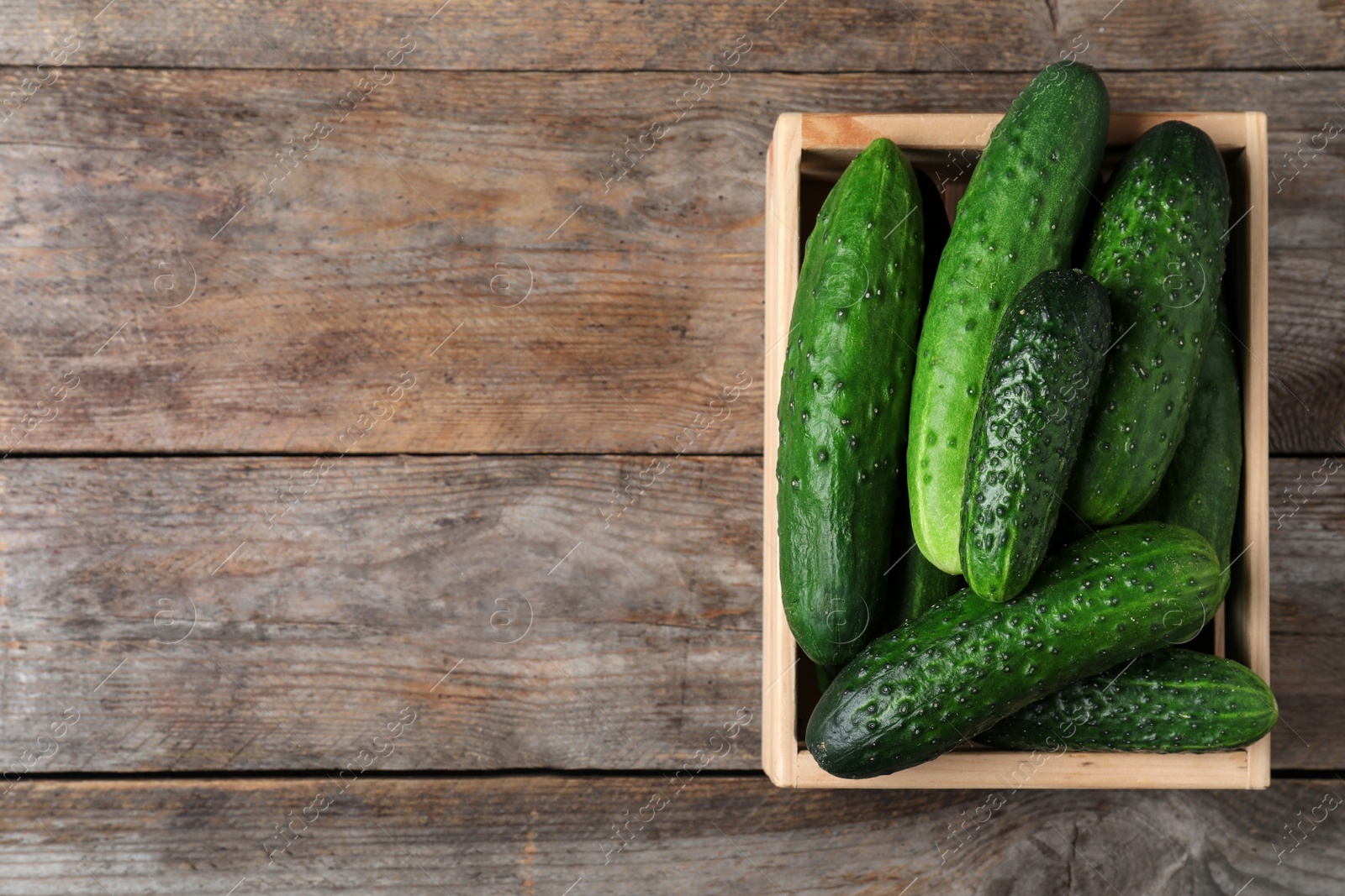 Photo of Crate full of fresh ripe cucumbers on wooden background, top view. Space for text