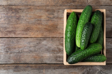 Crate full of fresh ripe cucumbers on wooden background, top view. Space for text