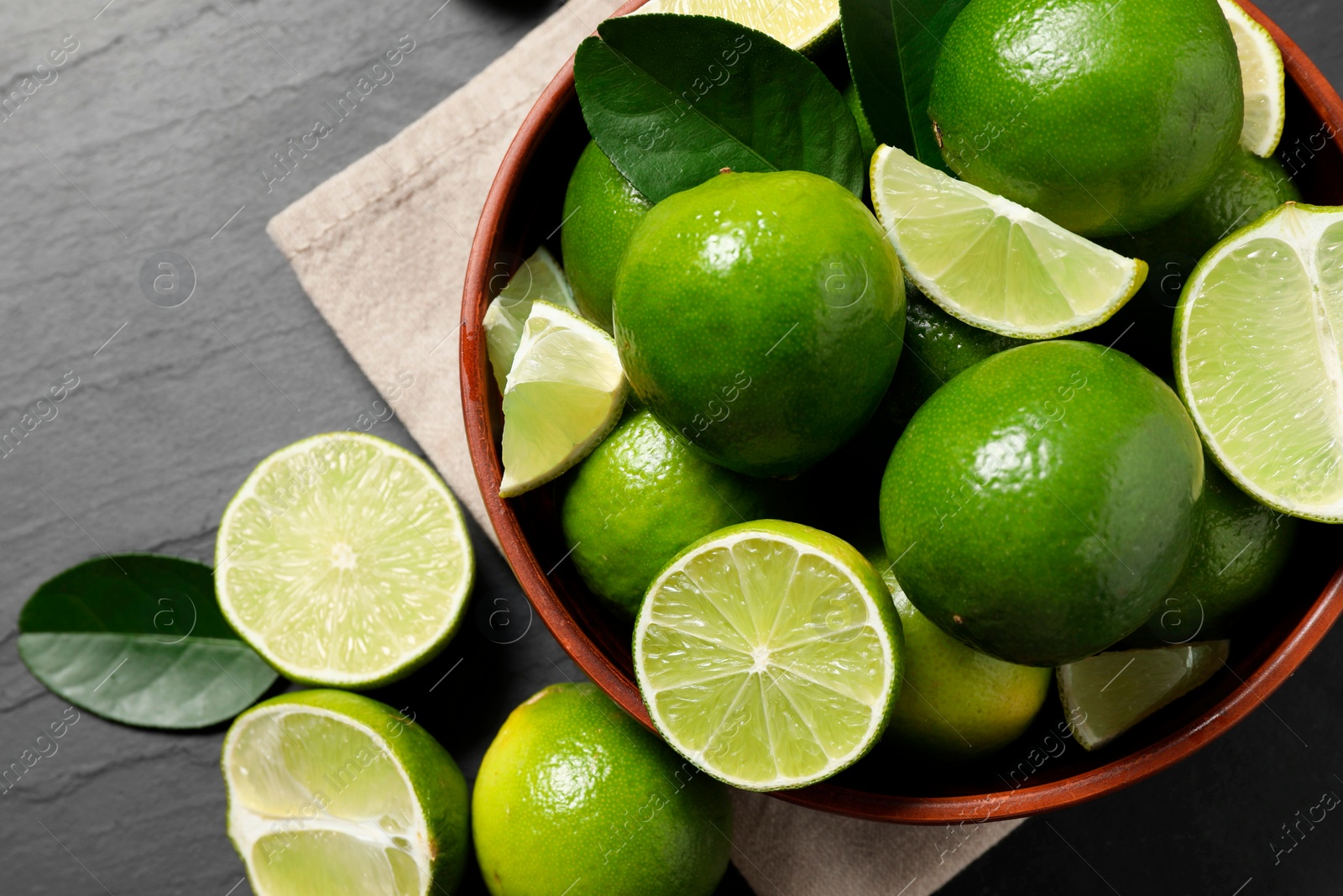 Photo of Fresh ripe limes in bowl on black table, top view