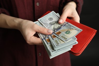Photo of Money exchange. Woman putting dollar banknotes into wallet on dark background, closeup